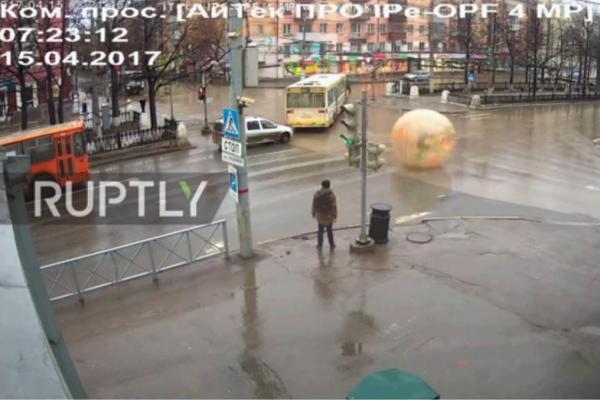 Sebuah rekaman CCTV menunjukkan seorang pria berjalan melewati kendaraan melintas dengan menggunakan balon air di sebuah kota di Rusia.